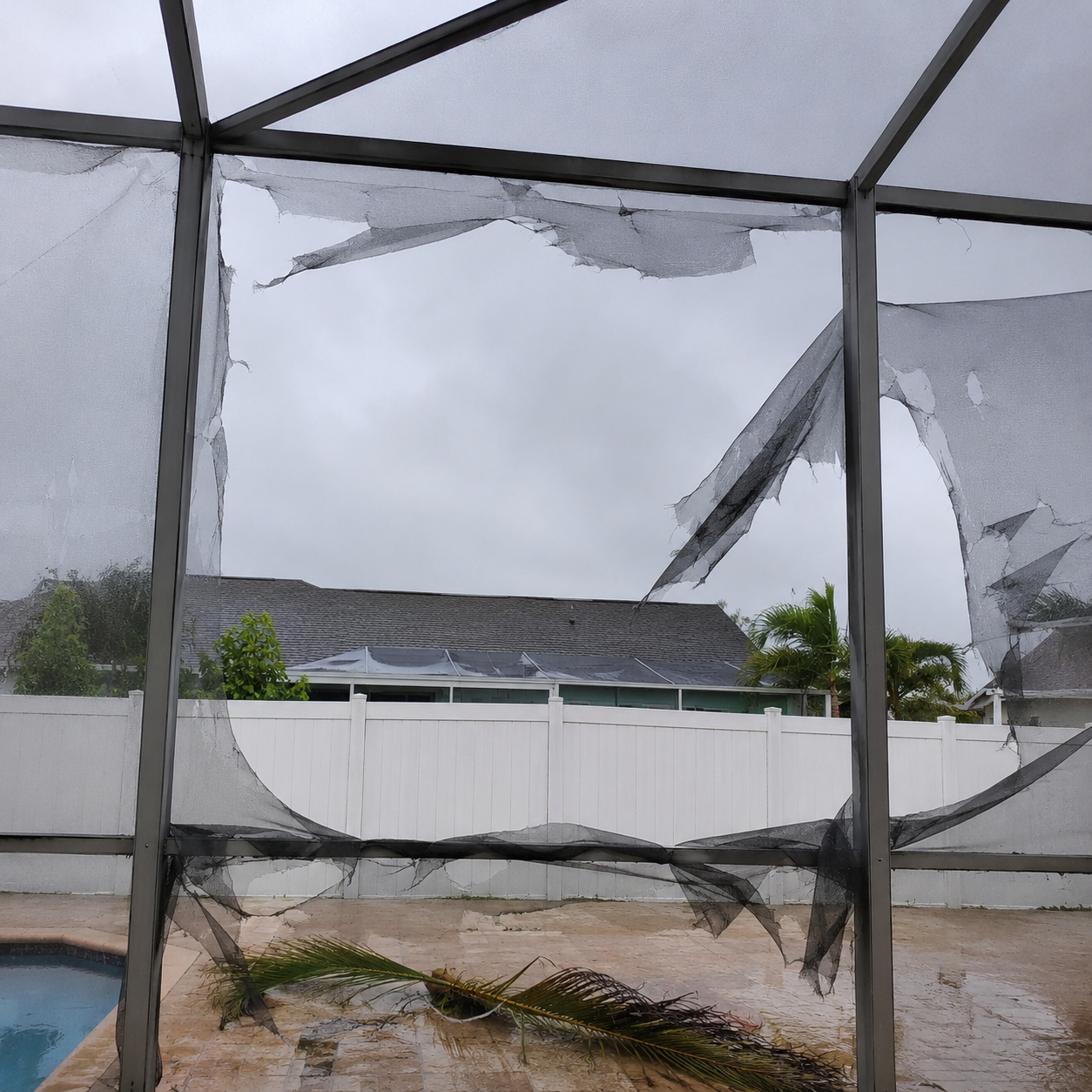 Pool cage screen panel severely torn by storm wind before repair